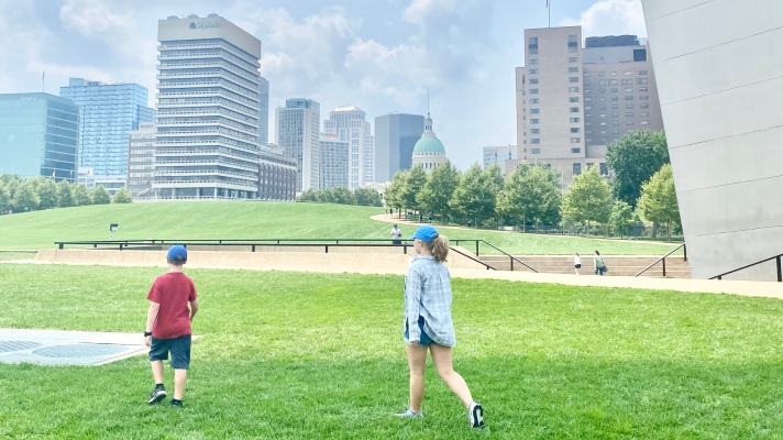 Two kids Playing in the grass at the Base of Gateway Arch National Park with a view of the old Capitol in the background 